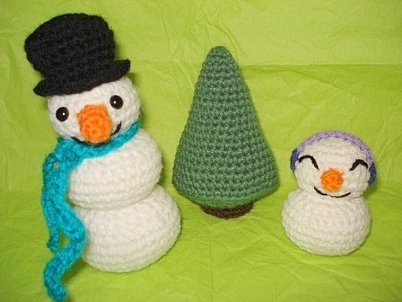 Zwei gehäkelte Schneemänner und ein grüner Tannenbaum auf hellgrünem Hintergrund