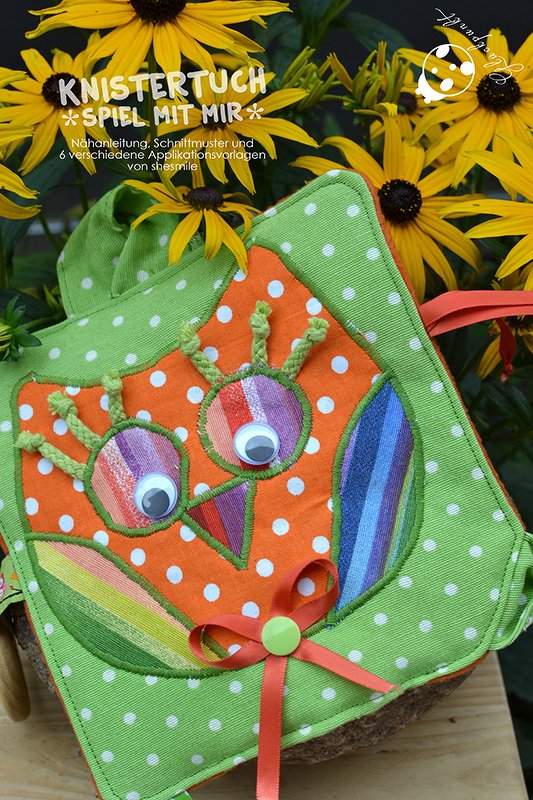 Selbstgenähtes, buntes Knistertuch in Eulenform mit Wackelaugen und weißen Punkten vor gelben Blumen