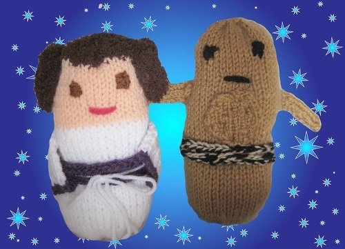 Zwei gestrickte Amigurumi-Puppen: weiße Puppe mit dunklem Haar und braune Puppe mit Taillenband vor sternenblauem Hintergrund