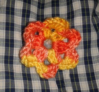 Gehäkelte Blume in Orange und Gelb auf blau-weiß kariertem Stoff