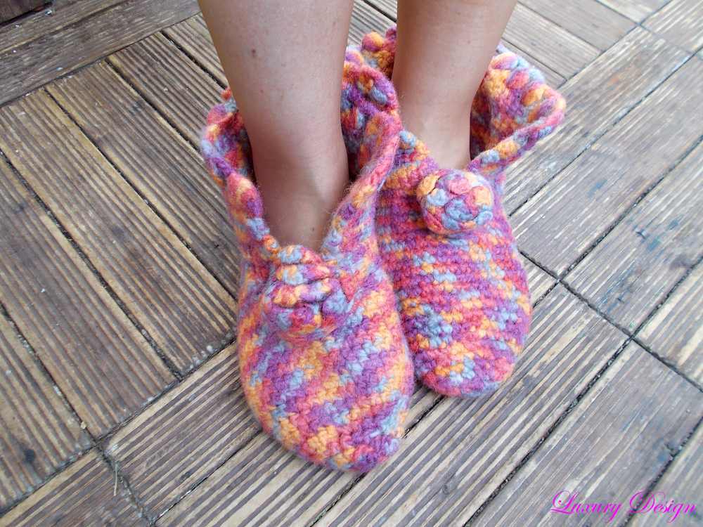 Mehrfarbige gehäkelte Hausschuhe mit Zierknopf auf Holzdielen