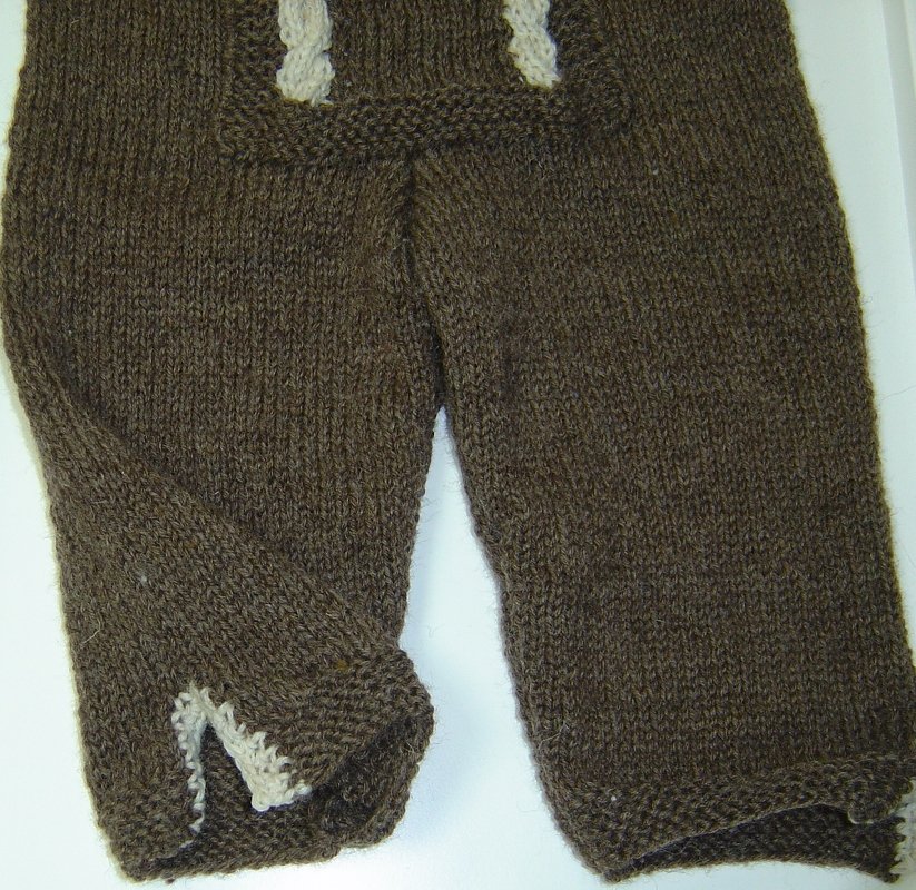 Dunkelbraune gestrickte Babyhose mit zwei hellen Zopfträgern und sichtbarer Maschenstruktur