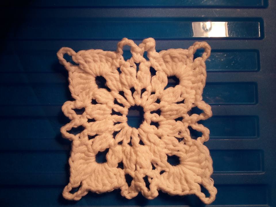 weißes gehäkeltes Granny Square mit offener Mitte und dekorativen Ecken auf blauem Grund