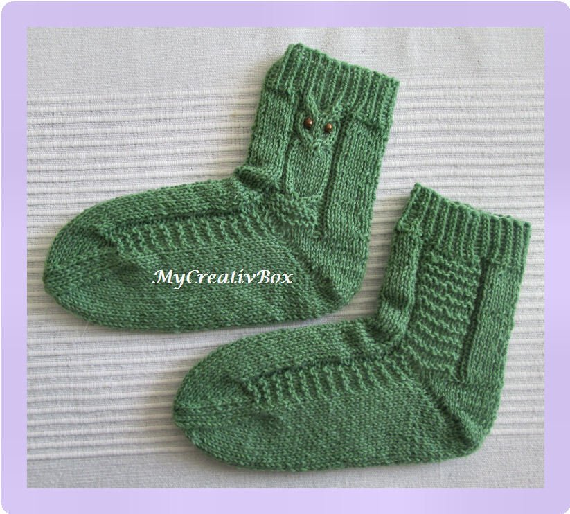 Zwei gestrickte grüne Babysocken mit geripptem Bündchen und Eulenmotiv