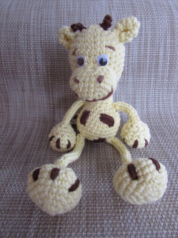 Hellgelbe gehäkelte Amigurumi‑Giraffe mit braunen Flecken und Wackelaugen, sitzend