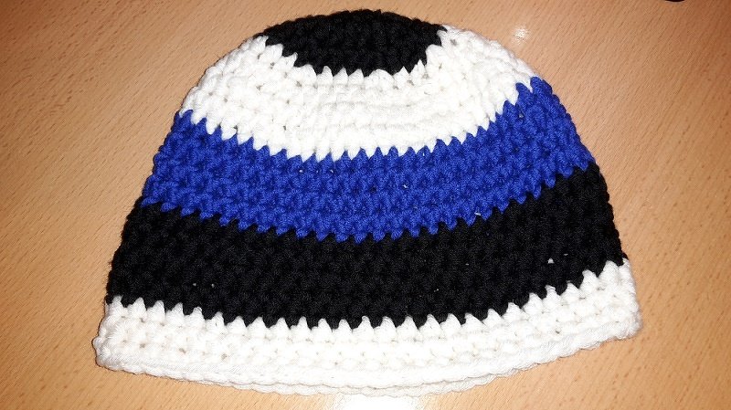 Gehäkelte, gestreifte Mütze in Weiß, Schwarz und Blau auf Holzuntergrund