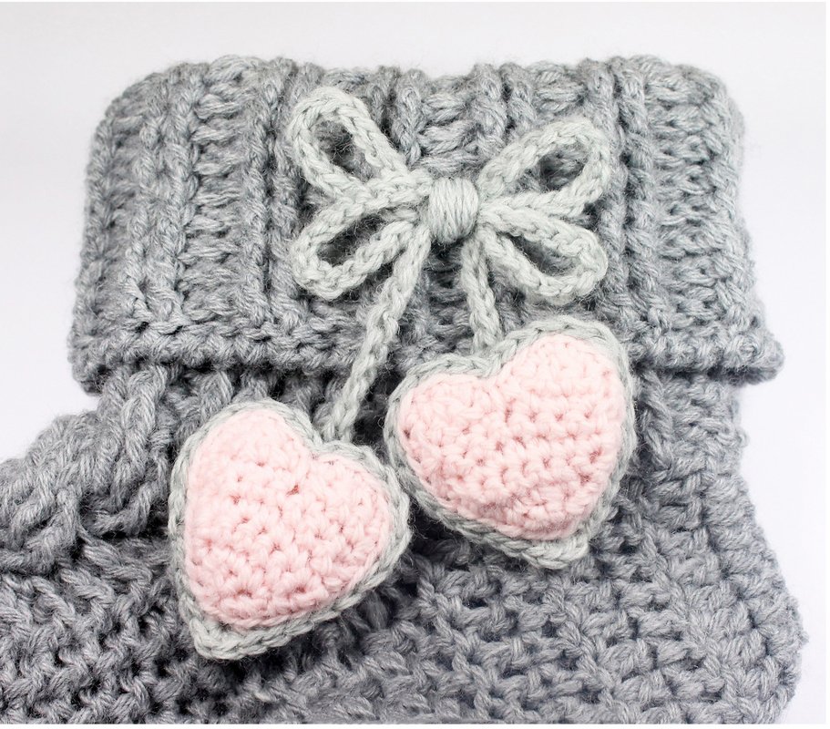Grau gehäkelte Socke mit rosa Herzen und grauer Schleife.
