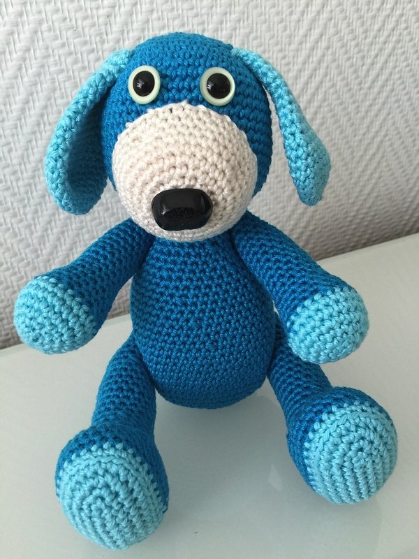 Blauer gehäkelter Amigurumi-Hund mit hellblauen Pfoten, heller Schnauze und schwarzer Nase