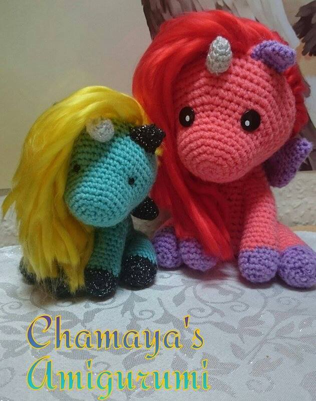 Zwei gehäkelte Einhörner, großes rosa Einhorn mit roter Mähne und violetten Hufen, kleines türkisfarbenes Einhorn mit gelber Mähne und dunklen Hufen