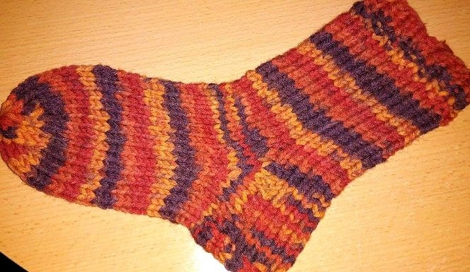 Gestreifte Stricksocke in Rot, Orange und Violett auf heller Holzfläche