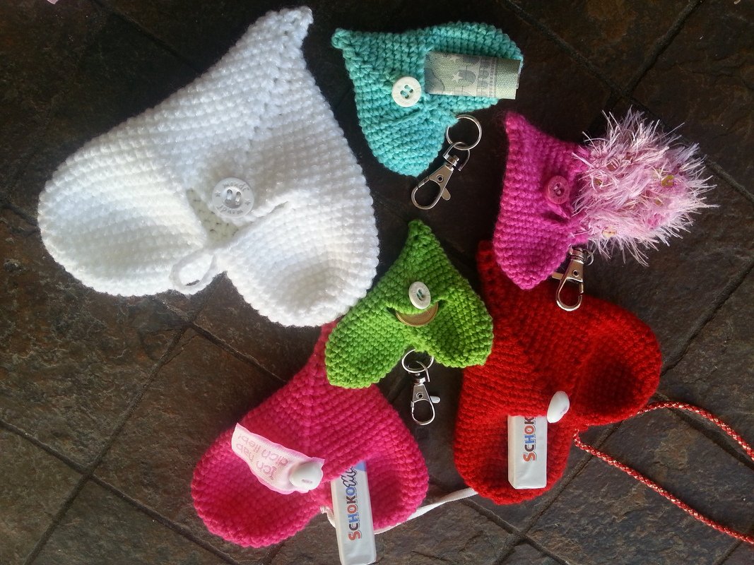 Mehrere gehäkelte Herz-Täschchen in Weiß, Pink, Rot, Grün und Türkis mit Knöpfen und Karabinern