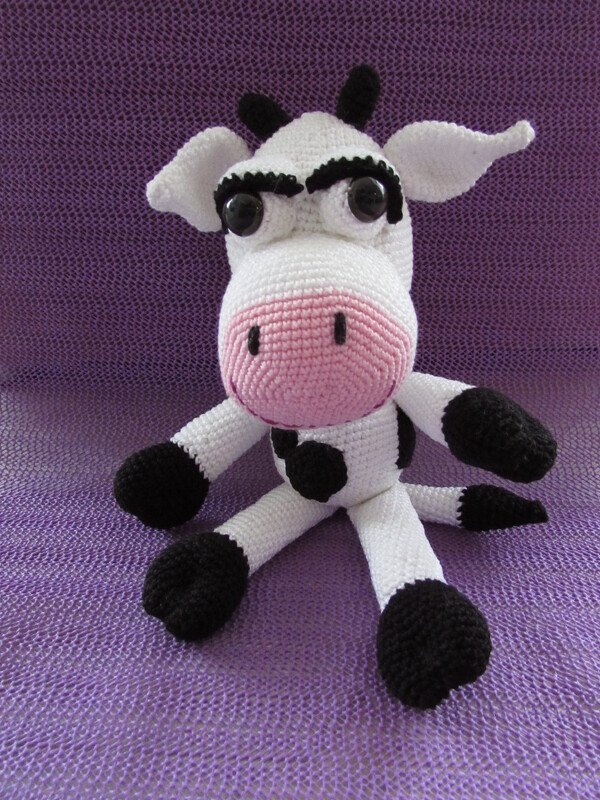 Gehäkelte Amigurumi Kuh in Weiß und Schwarz mit rosa Schnauze auf violettem Hintergrund