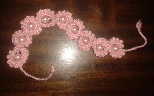 Reihe aus rosa gehäkelten Blüten mit Perlen und Bindebändern