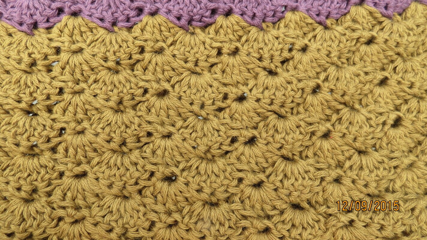 Nahaufnahme eines gehäkelten senfgelben Musters mit Büschelmaschen und lila Rand