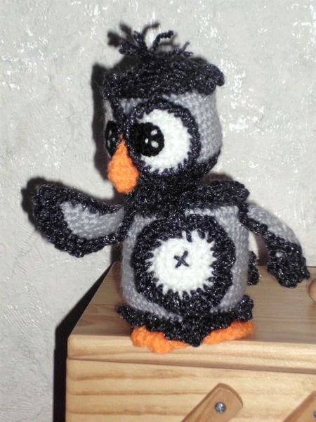 Gehäkelte Amigurumi-Eule in Grau, Schwarz und Orange auf einem Holzregal.