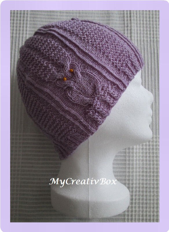 lila gestrickte Beanie mit Zopfmuster und Eulenapplikation auf Schaufensterkopf