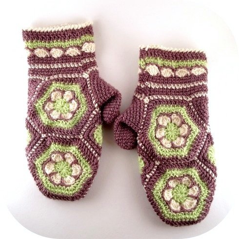 Handgehäkelte Fäustlinge in Lila, Hellgrün und Creme mit sechseckigen Blumenmotiven und texturierten Bündchen.