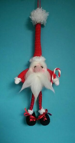 Gehäkelter Weihnachtsmann-Amigurumi mit langer roter Zipfelmütze, weißem Bart und Zuckerstange, hängend vor blauem Hintergrund