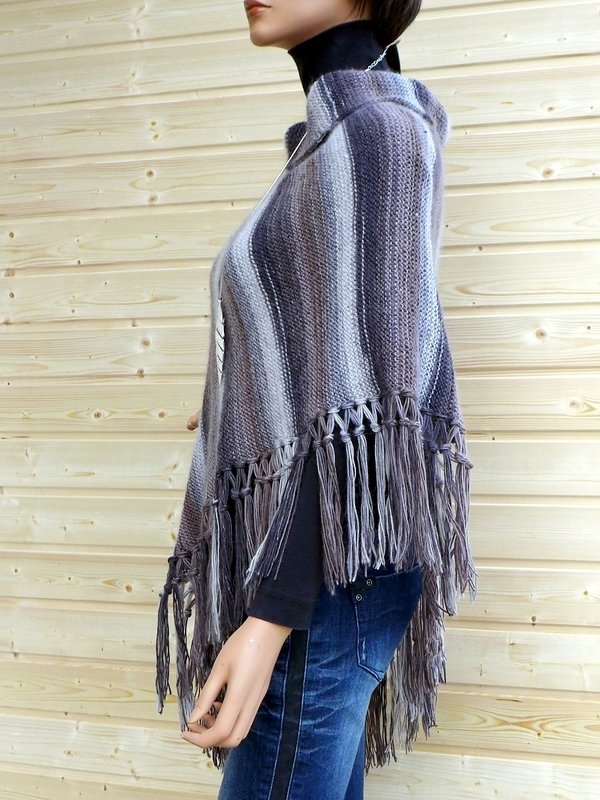 Gestrickter Poncho in Grau- und Lilatönen mit Fransen an einer Schaufensterpuppe vor Holzverkleidung.