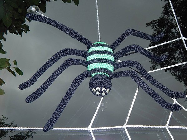 Gehäkelte Amigurumi-Spinne in Schwarz und Grün, hängend an einem gehäkelten Netz