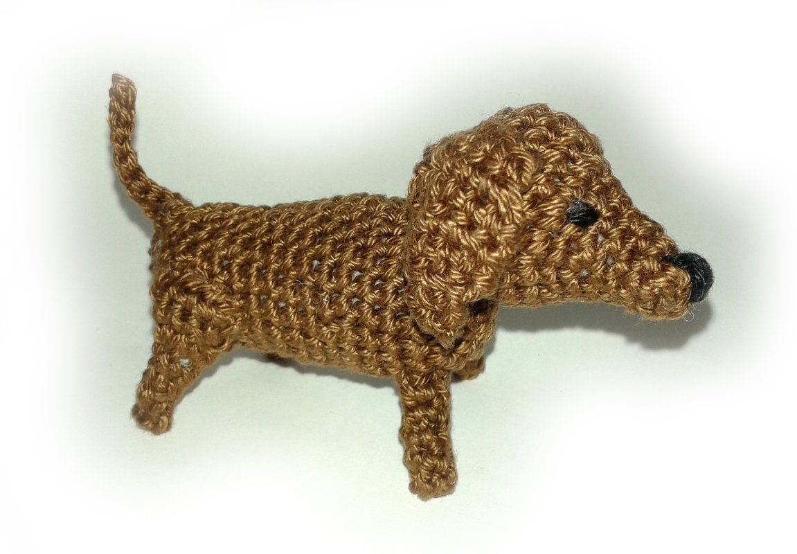 Brauner gehäkelter Amigurumi-Dackel mit schwarzen Augen und Nase auf weißem Hintergrund