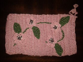 Rosa gehäkeltes Täschchen mit drei Blumenapplikationen, grünen Blättern und Perlen