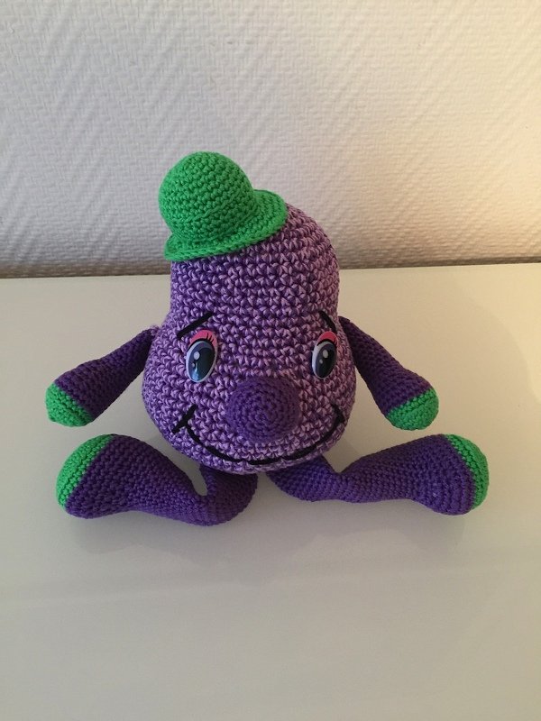 Gehäkeltes lila Amigurumi mit grünem Minihut und applizierten Augen