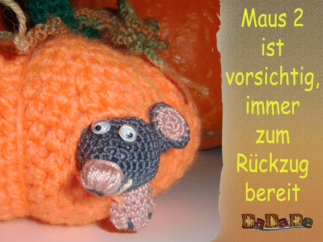 Gehäkelte graue Maus mit rosa Ohren schaut aus einem orangefarbenen Häkelkürbis