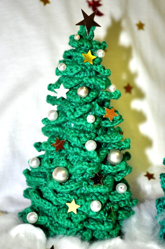 Gehäkelter grüner Mini-Weihnachtsbaum mit Perlen und Stern-Pailletten auf weißer, schneeähnlicher Unterlage.
