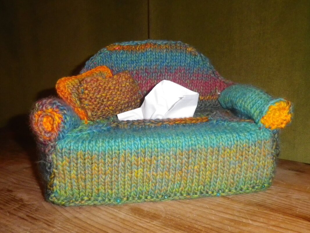 Gestrickter Taschentuchbox-Bezug in Sofaform, bunt, mit Zierkissen und weißem Taschentuch