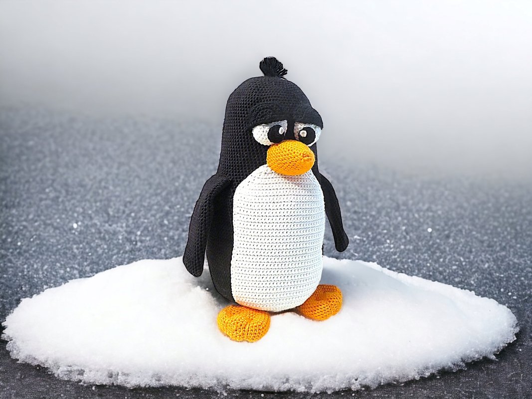 Close view of a crocheted penguin amigurumi highlighting white belly and orange beak