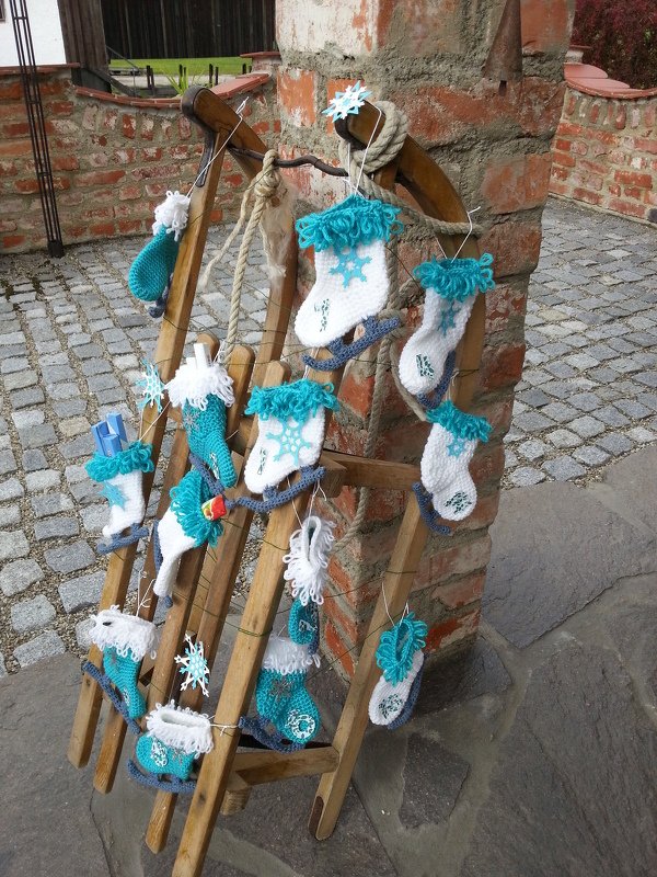 Holzschlitten mit gehäkelten weißen und türkisen Mini-Socken als Adventskalender-Anhänger