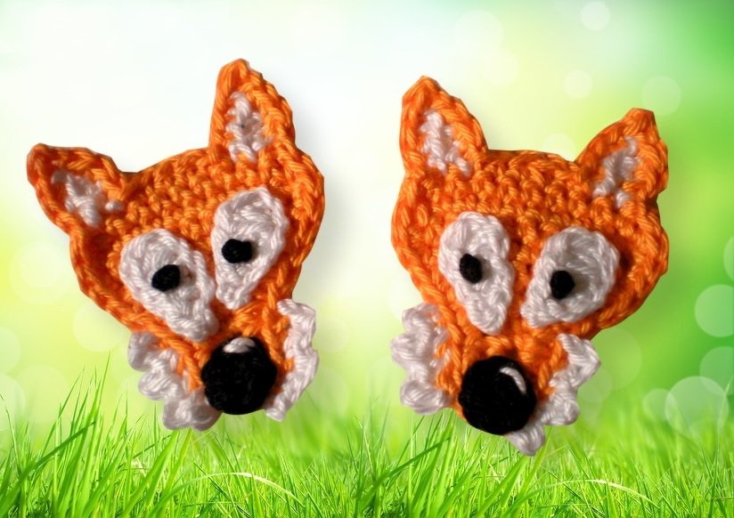 Zwei gehäkelte Fuchs-Applikationen in Orange und Weiß auf grünem Hintergrund