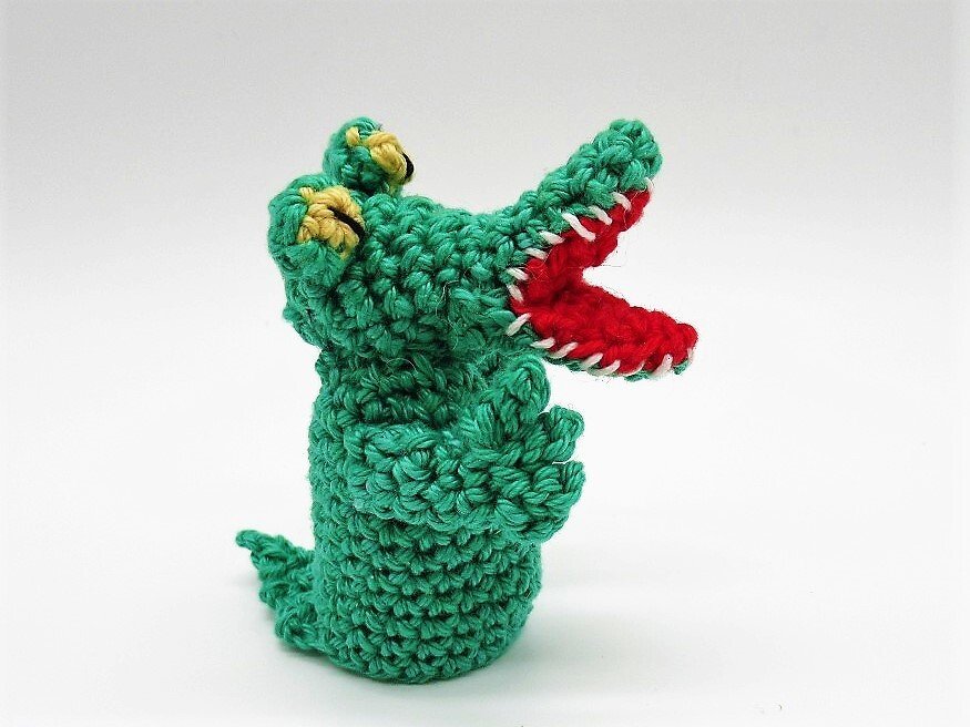 Grüne gehäkelte Krokodil-Fingerpuppe mit rotem Maul und gelben Augen