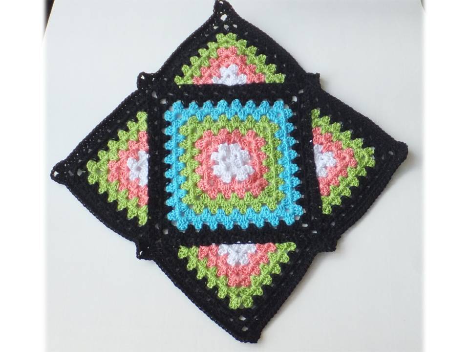 Gehäkeltes Granny Square mit weißem Zentrum, pinken, grünen und türkisen Ringen und schwarzem Rand