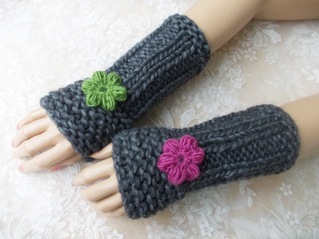 Dunkelgraue gestrickte Armstulpen mit grüner und pinker Blumenapplikation auf Modellhänden