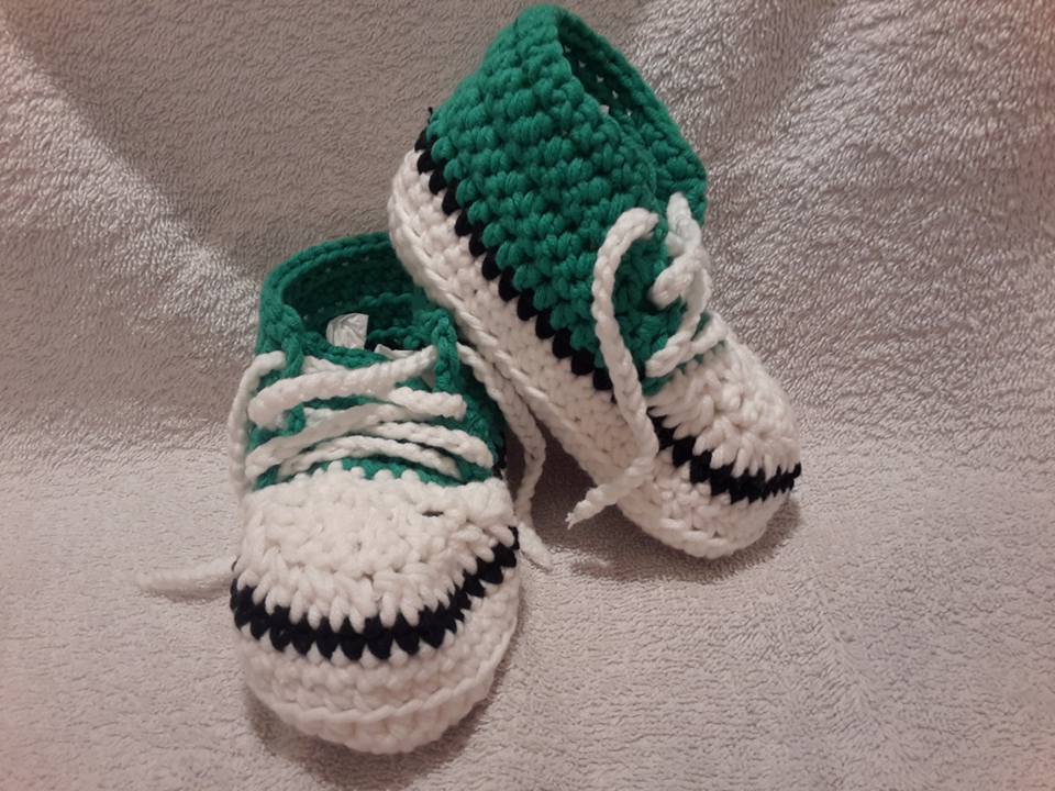 Gehäkelte Babysneaker in Grün, Weiß und Schwarz mit weißen Schnürsenkeln auf hellem Untergrund
