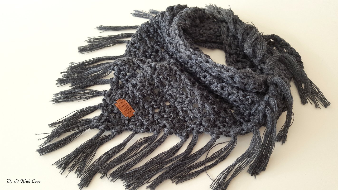 Dunkelgraues gehäkeltes Dreieckstuch mit langen Fransen auf hellem Hintergrund