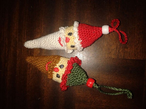 Zwei gehäkelte Wichtel-Schlüsselanhänger, rot-weiß und braun-grün, auf dunklem Holz