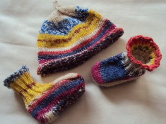 Gestrickte Babymütze und zwei Schühchen mit bunten Streifen auf hellem Untergrund