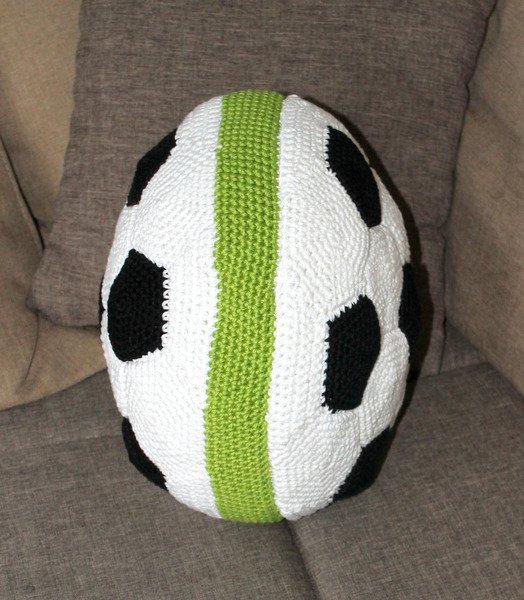 Hand-crocheted soccer ball pillow with a vertical green stripe on a couch.