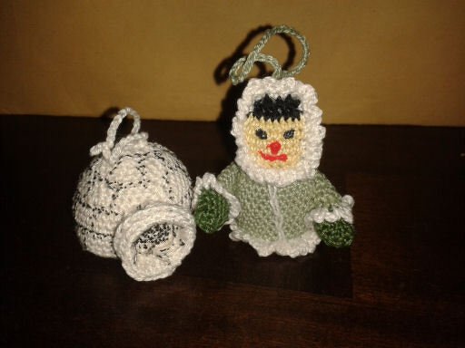 Zwei gehäkelte Schlüsselanhänger: grüne Kapuzenfigur und weißer glockenförmiger Anhänger mit Schlaufen
