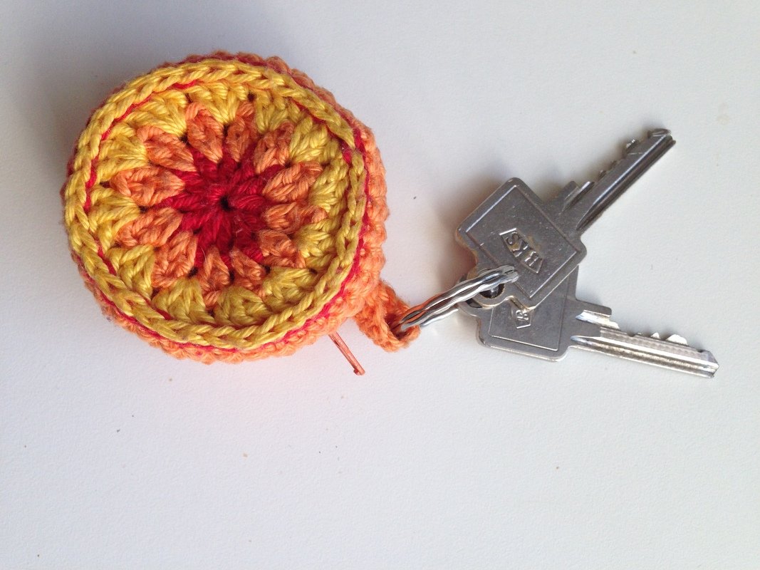 Kleines rundes gehäkeltes Etui in Gelb-Orange am Schlüsselring mit zwei Schlüsseln auf heller Fläche