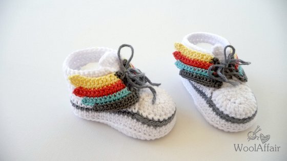 Gehäkelte weiße Babyschuhe mit grauer Sohle und bunten Flügeln an der Seite