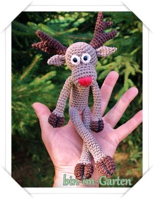 Gehäkelte Rentier-Fingerpuppe mit roter Nase in einer offenen Hand vor Tannengrün