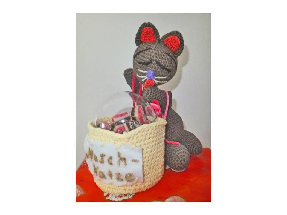 Gehäkelte graue Amigurumi-Katze neben beigem Körbchen mit klarer Abdeckung