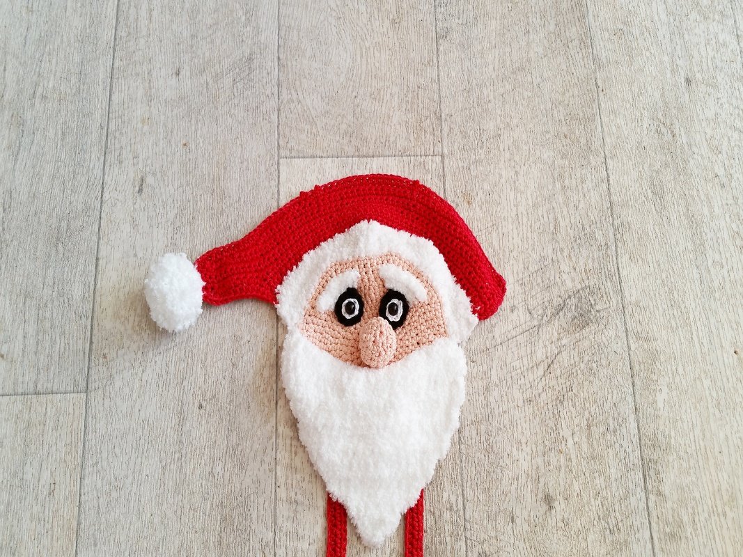 Gehäkelter Weihnachtsmannkopf mit roter Mütze und weißem Bart auf hellem Holzboden