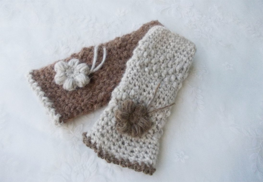 Gehäkelte, fingerlose Armstulpen in Beige und Braun mit Blumenapplikationen auf hellem Untergrund