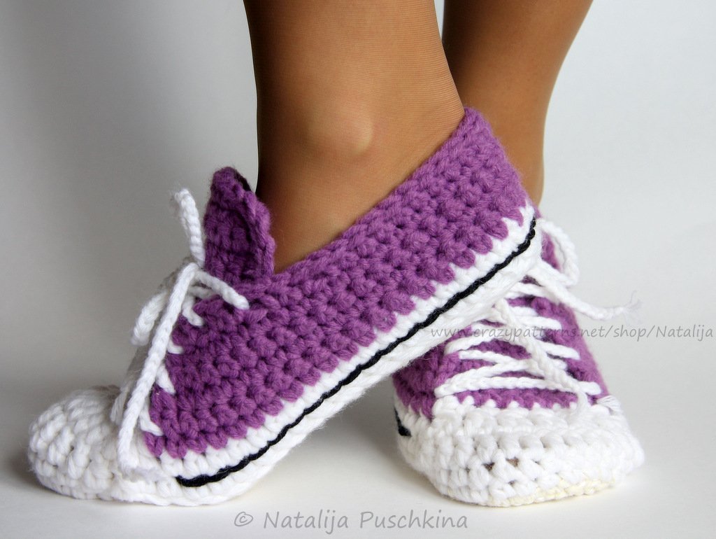 Close-up of feet wearing purple and white crocheted sneaker-style slippers with white laces.