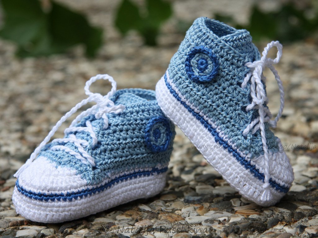 Pair of blue and white crocheted baby sneakers with white laces on a pebble surface